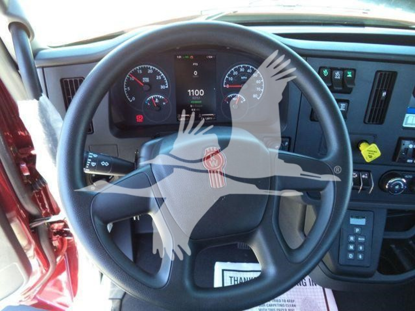 Dashboard view of a Kenworth truck steering wheel with instrument cluster and control panels visible, featuring a center digital display and multiple gauges.