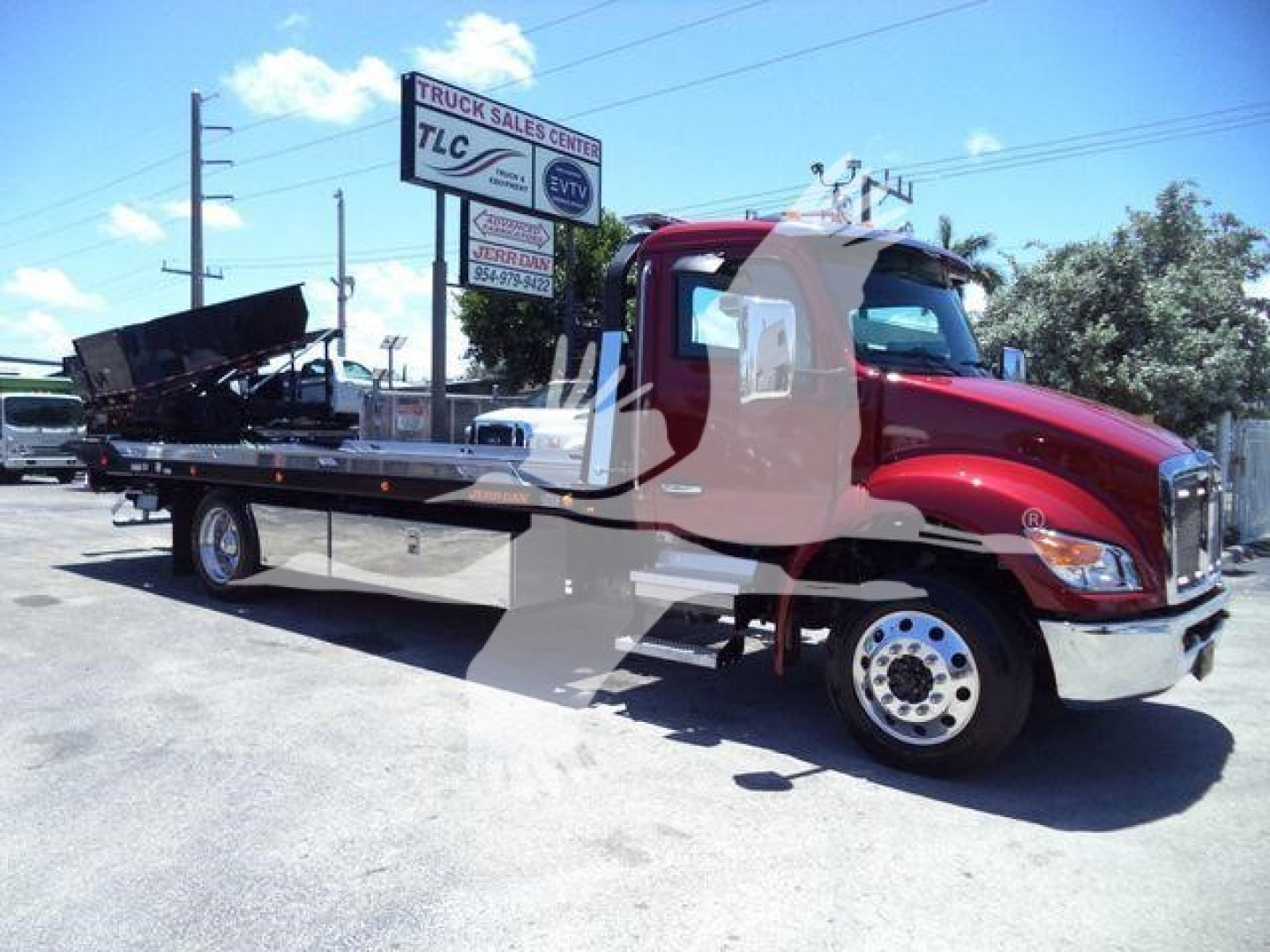 Kenworth T280 rollback truck with flatbed, red cab, viewed side-on; stock signage in background.