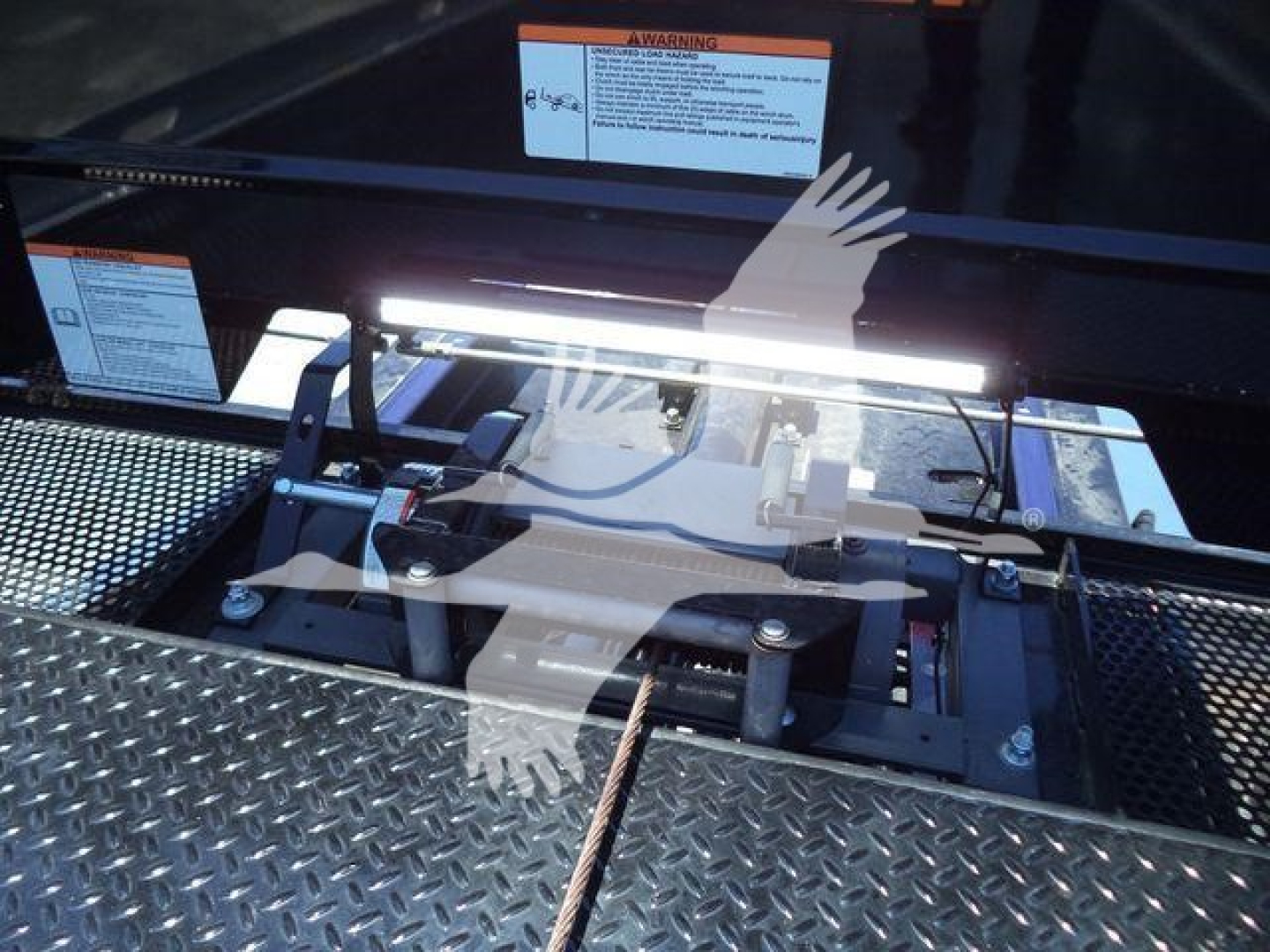 Kenworth T280 rollback tray with control bar and wiring visible; metallic diamond plate surface; warning labels and bright LED work light across top edge.