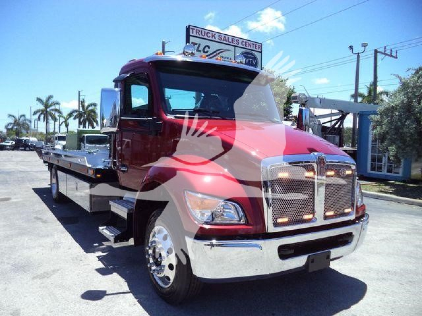 Truck front left view of Kenworth T280 rollback with maroon cab and chrome grille. Text on sign above: not legible. No visible fluid labels or details other than generic truck features.