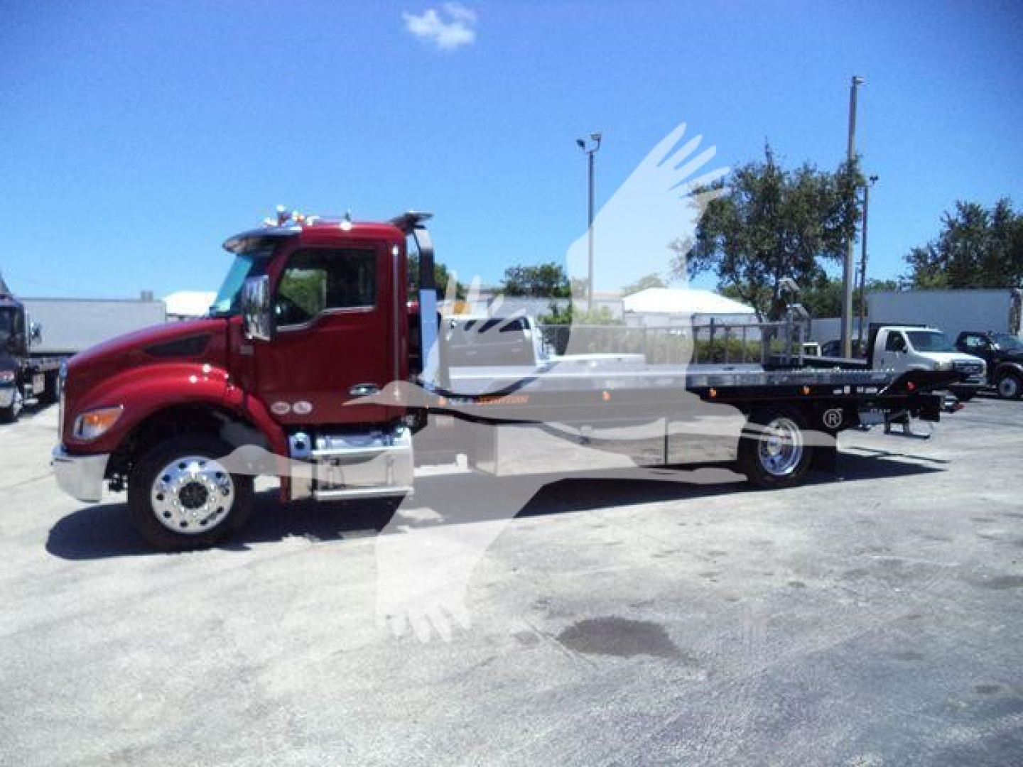 Kenworth T280 rollback truck in red cab with flatbed, side view showing wheel hubs, chrome exhaust, and white lettering on truck.