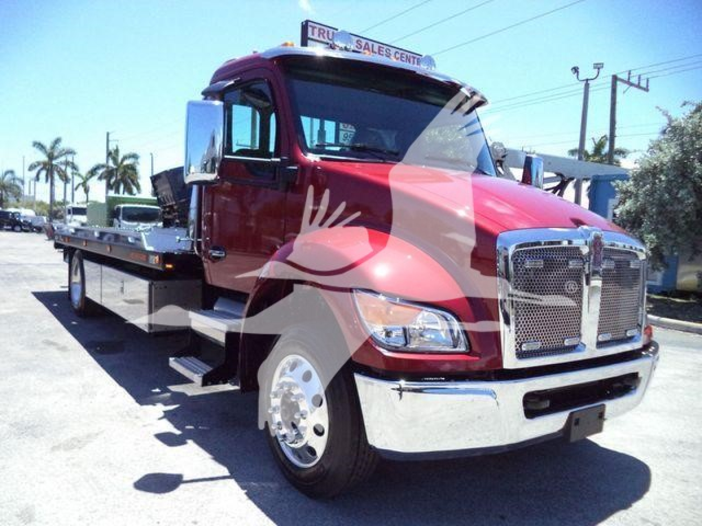 Kenworth T280 rollback truck with red cab and chrome grille, side platform, and dual side mirrors. Text not legible from image.