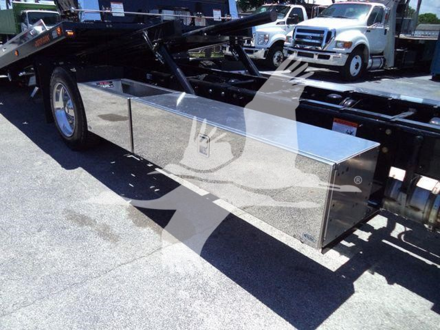 Truck flatbed toolbox mounted under frame of Kenworth T280 rollback truck, chrome aluminum rectangular toolbox with polished finish.