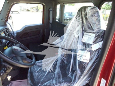 Truck cab interior showing wrapped driver seat and steering wheel; plastic-wrapped seats with labels attached.