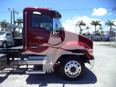 Truck side view showing front cab of a red 2025 Kenworth T280 with chrome wheel, fuel/alcohol tanks, and rollback chassis visible.