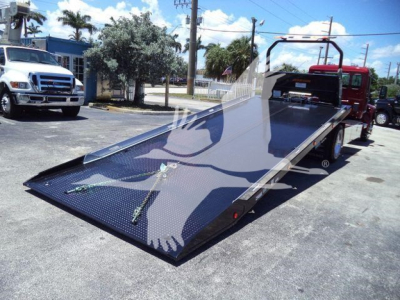 Kenworth T280 rollback truck with a lowered flatbed trailer in a dealership lot, reflective surface, white and blue exterior, truck cab visible in distance