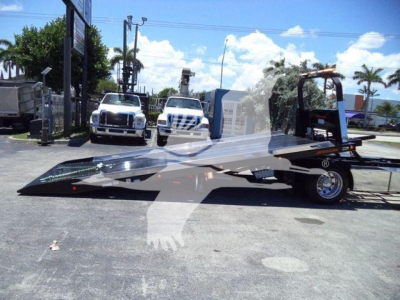 Kenworth T280 rollback truck in foreground with flatbed and ramps, dealership lot in background.