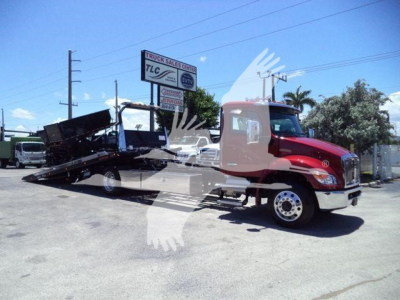 Kenworth T280 rollback truck in a dealership lot with flatbed bed extended, side view showing cab and utility equipment.