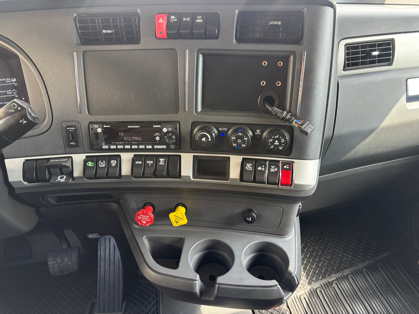 Kenworth T680 truck interior dashboard view showing center stack with climate controls, media head unit, several switches, cup holders, and ignition area.