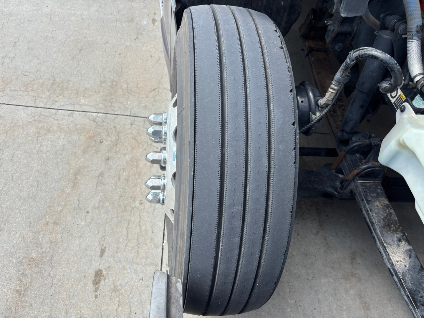 Kenworth T680 front wheelview showing multiple lug studs and tire; part of the front axle and braking/steering components visible.