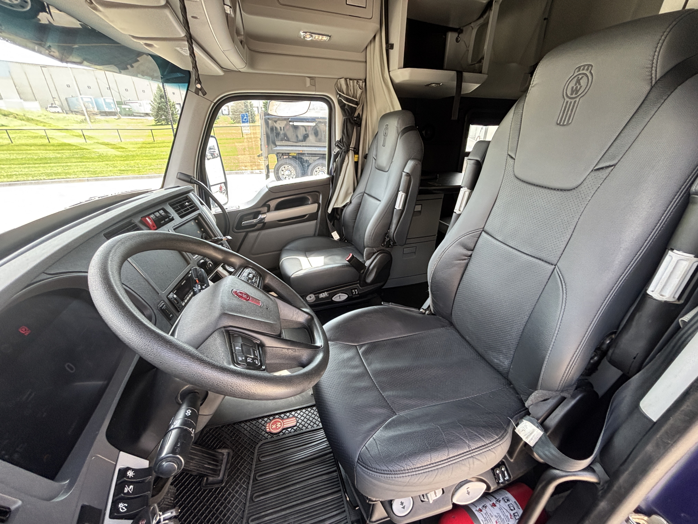 Interior of a Kenworth T680 cab showing driver seat and passenger seat with steering wheel and dashboard in view