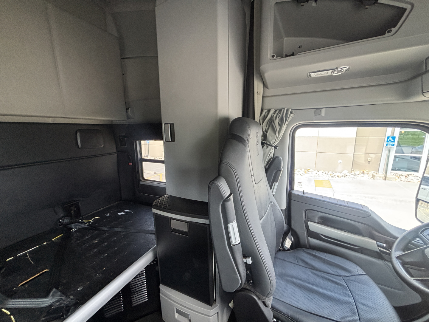 Kenworth T680 interior cab sleeper area with overhead compartments and driver seat, side window, and bunk area in view.