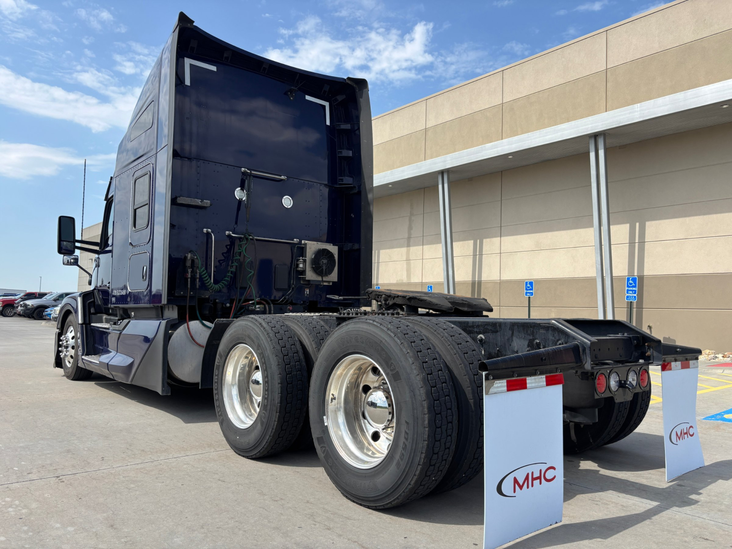 Kenworth T680 tractor rear view showing dual rear axles and chassis with mud flaps and dealership flags.