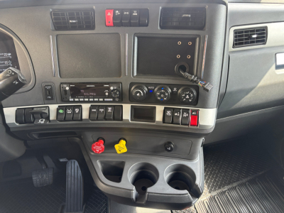Kenworth T680 truck interior dashboard view showing center stack with climate controls, media head unit, several switches, cup holders, and ignition area.