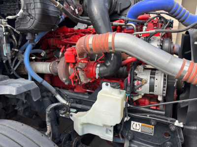 Kenworth T680 engine bay showing red engine block, large silver intercooler pipe, coolant reservoir, and blue hoses.