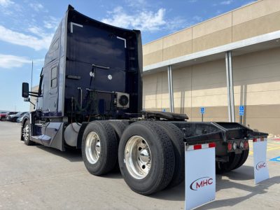 Kenworth T680 tractor rear view showing dual rear axles and chassis with mud flaps and dealership flags.
