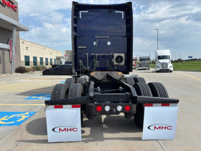 Kenworth T680 tractor rear view showing fifth wheel, dual rear axles, mud flaps with MHC logo, and white wheel fenders.