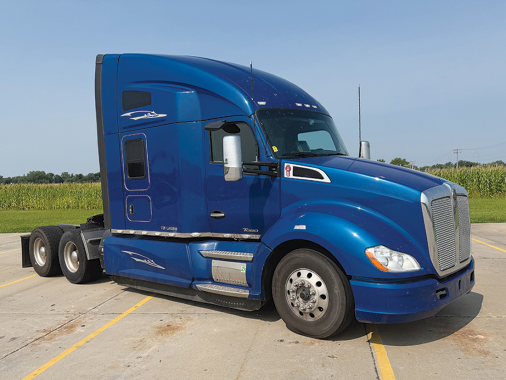 Kenworth T680 cab and wheel area in blue with sleeper, side tank steps, and dual rear axles visible.
