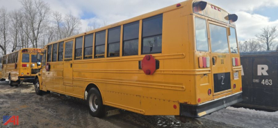 Rear and side view of a yellow Freightliner B2B school bus parked with another bus behind; back of bus shows tail lights, rear bumper, and a red circular hazard device on the side.