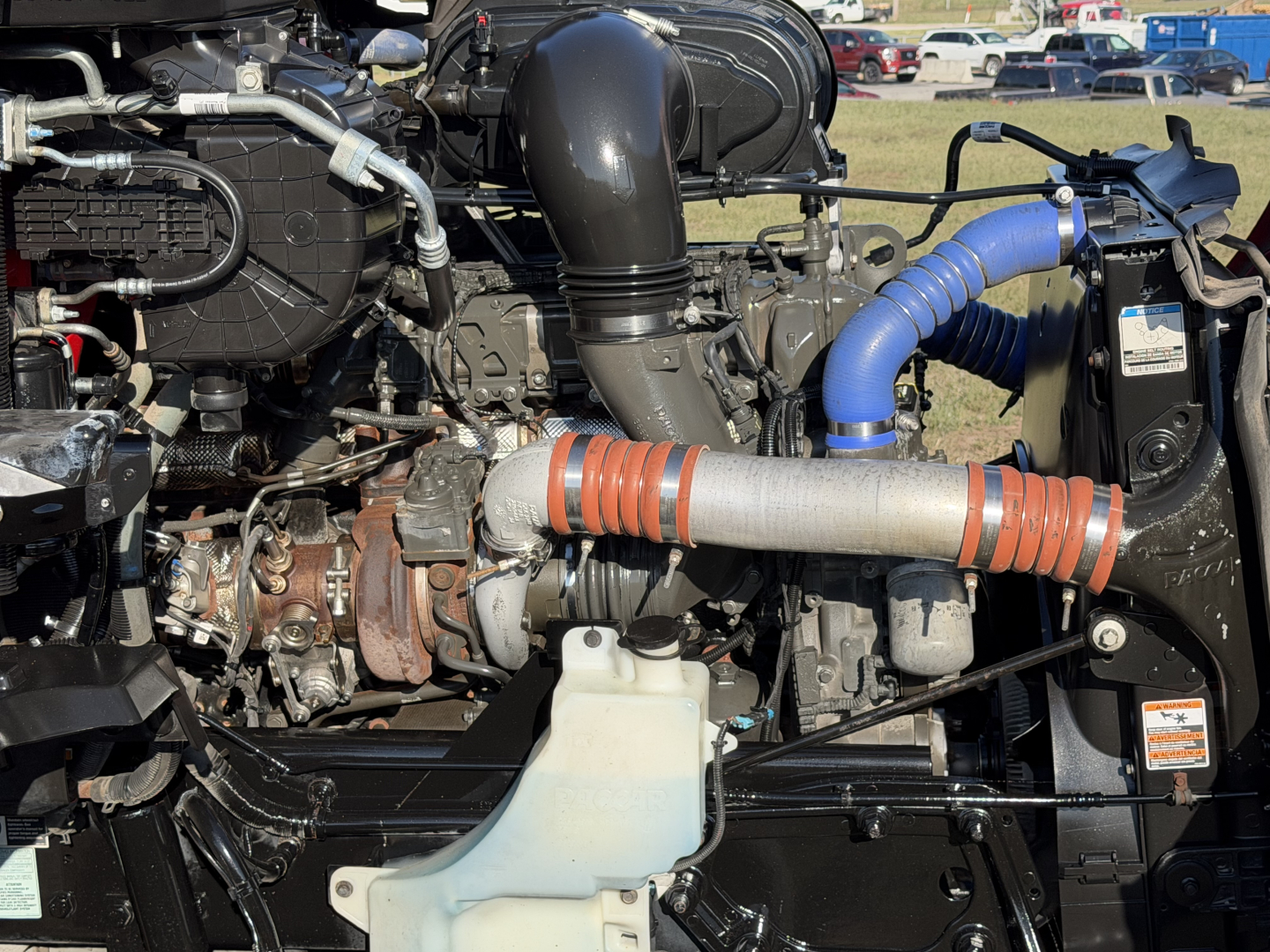 Kenworth T680 engine bay showing various hoses, intercooler piping, turbo, and coolant reservoir.