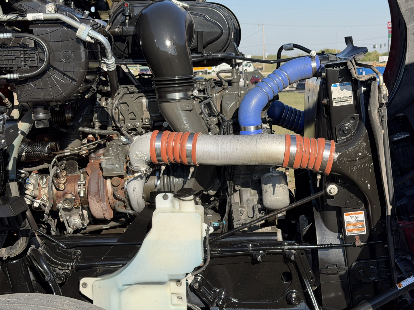 Kenworth T680 engine bay with visible turbocharger, intercooler piping, coolant reservoir, and various hoses and hoses clamps.