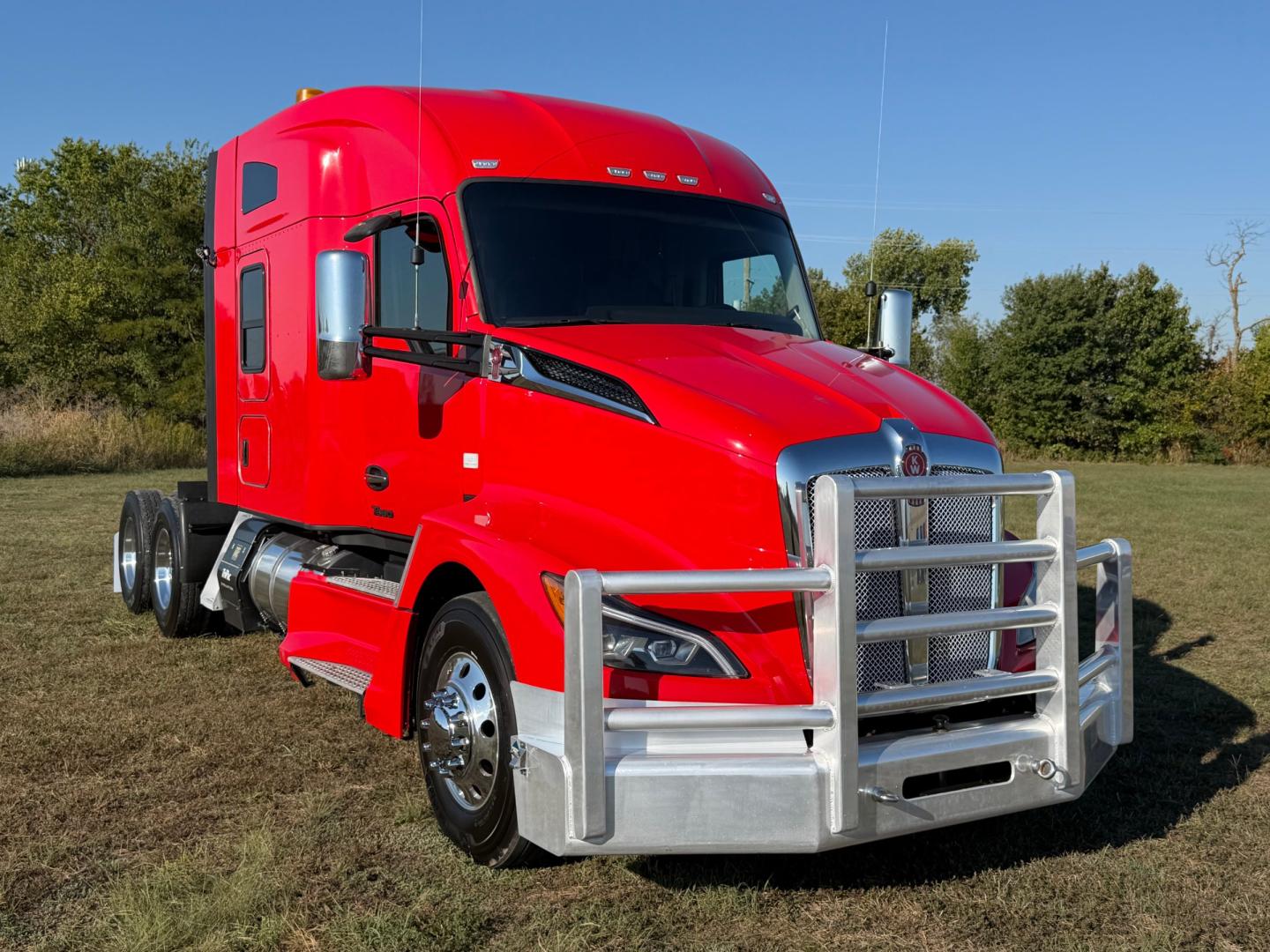 Kenworth T680 truck shows front grille guard and red sleeper cab with chrome bumper and dual mirrors.