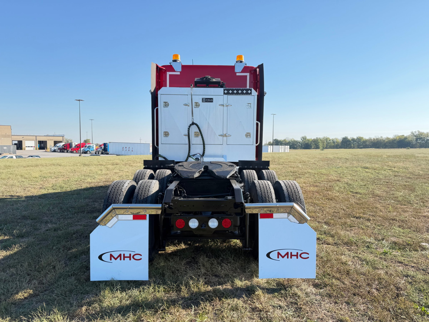 Kenworth T680 rear view showing dual rear axles and white mudflaps with MHC logos.