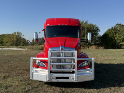 Kenworth T680 front view with large chrome grille guard, red cab, and silver bumper; no legible text visible on the truck’s grille.