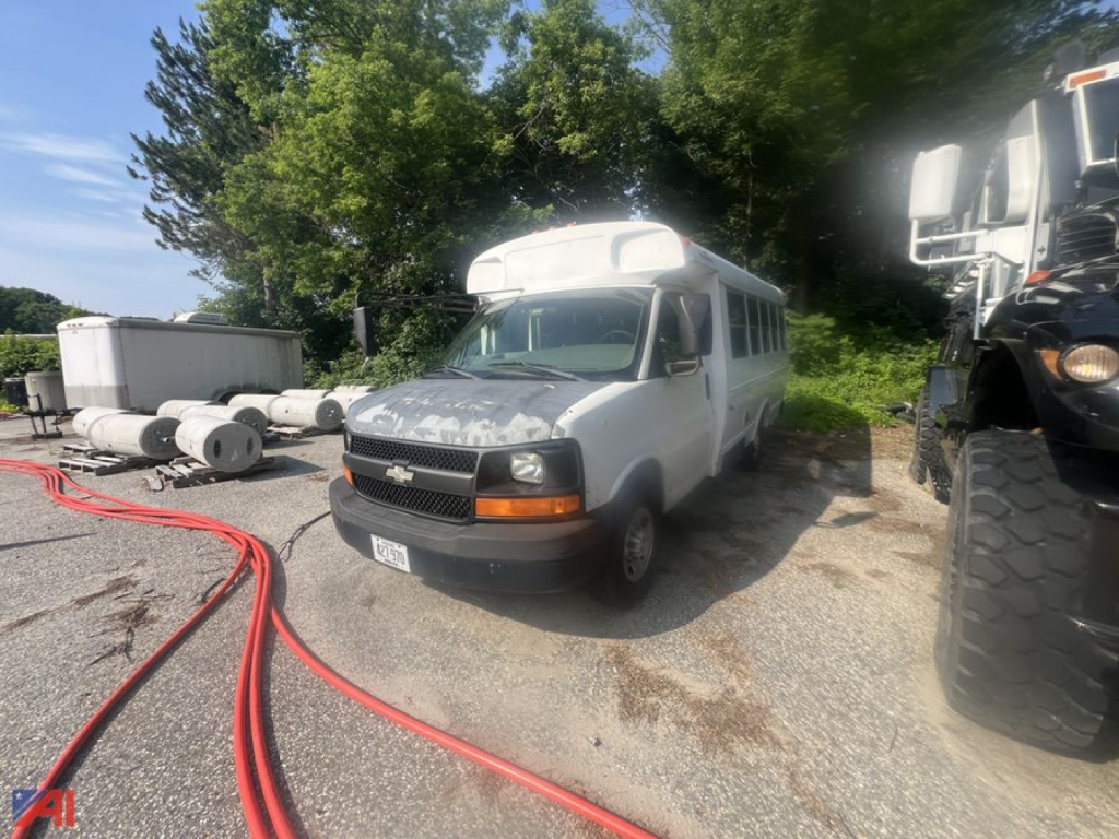 Chevrolet Express passenger bus 2003 in lot with roof air unit, front grille and headlights visible, hoses on ground nearby.