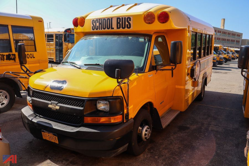 School bus showing front view with bright yellow body and 'SCHOOL BUS' sign on top; Chevrolet logo on grille and black bumper; side mirrors and exit door visible.