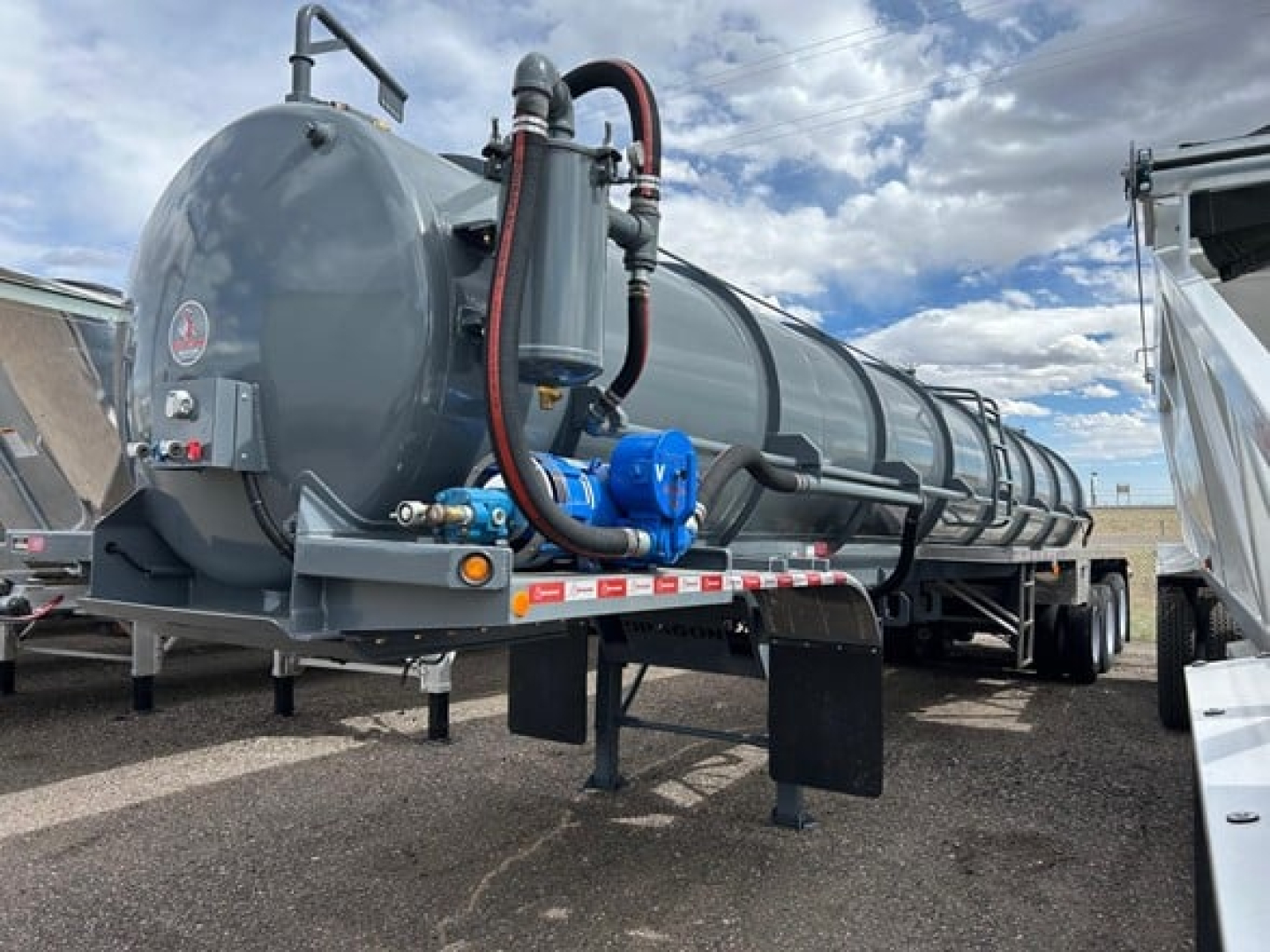 Trailer vacuum tanker showing cylindrical tank with hoses and blue pump assembly, connected piping, and support legs.