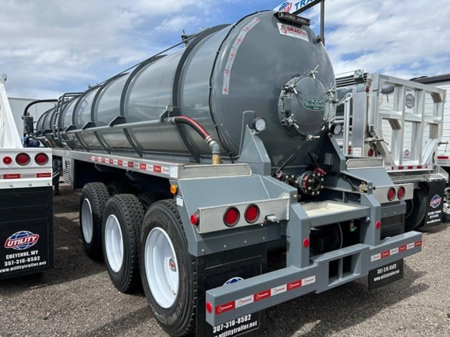 Vacuum trailer in-service showing cylindrical tank with rear feed connections and dual rear axles. Visible labels and hoses on tank rear end.