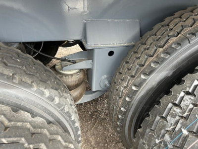 Trailer chassis showing dual rear wheels and suspension with coil spring, grey frame, and leaf-like components visible near wheel hub.