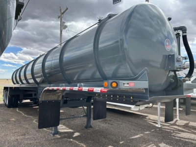 Vacuum trailer on trailer frame, cylindrical stainless tank with black hosing and support legs visible