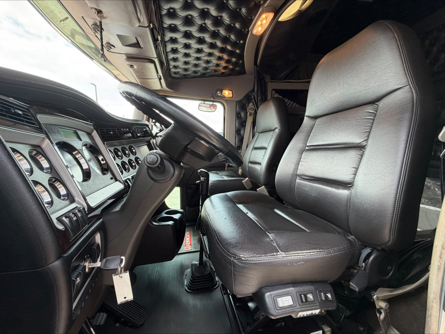 Kenworth W900L truck interior showing driver seat and steering wheel with dashboard gauges; caller notes may include VIN label and controls.