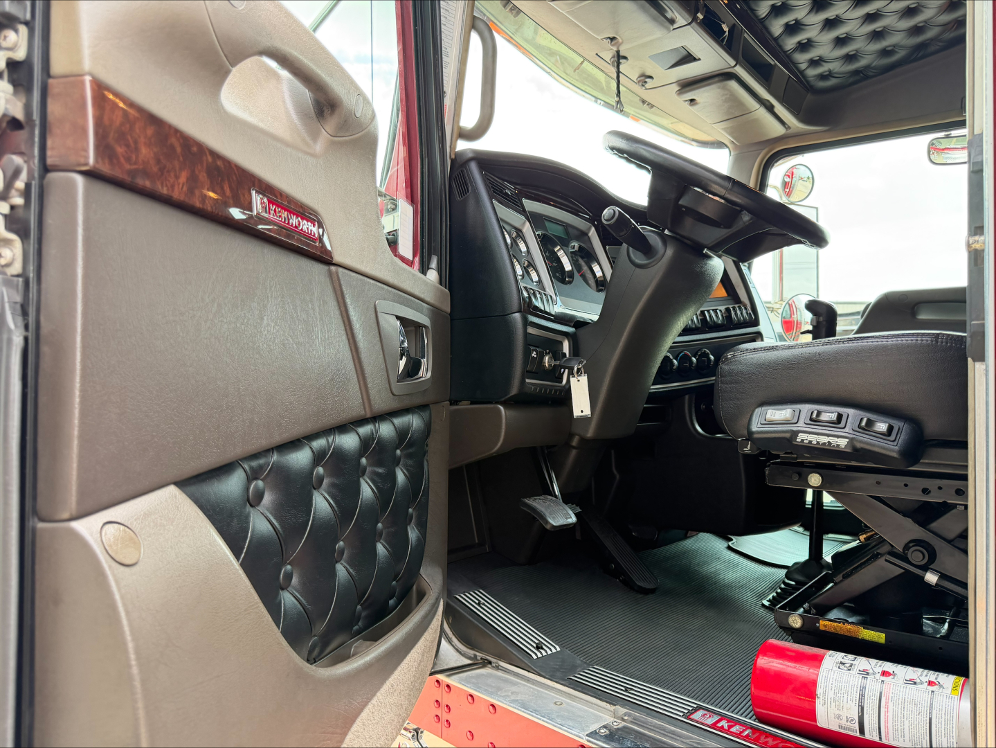 Kenworth W900L truck interior showing driver seat, dashboard, steering wheel, and open door with diamond-stitched door panel.