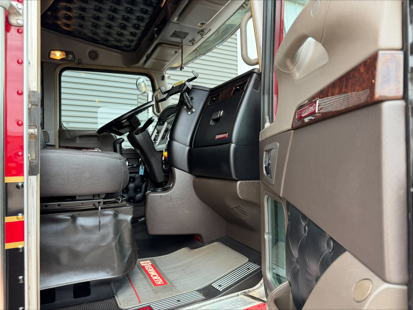 Kenworth W900L truck interior showing driver seat and dashboard area with Kenworth logo on door panel and textured mat.