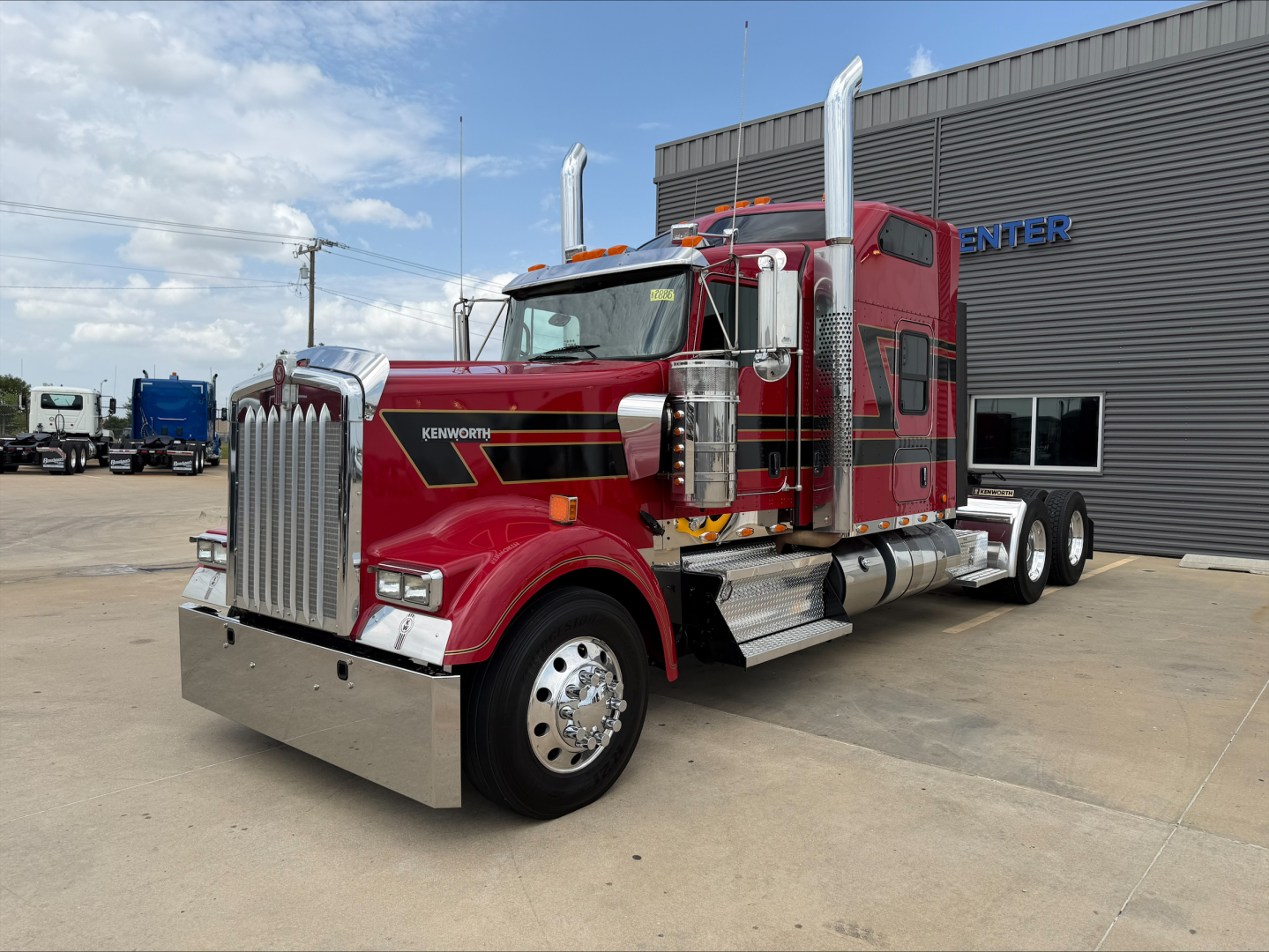 Kenworth W900L conventional sleeper truck in red, front grille, dual chrome exhaust stacks, large bumper, chrome wheels, and side steps.