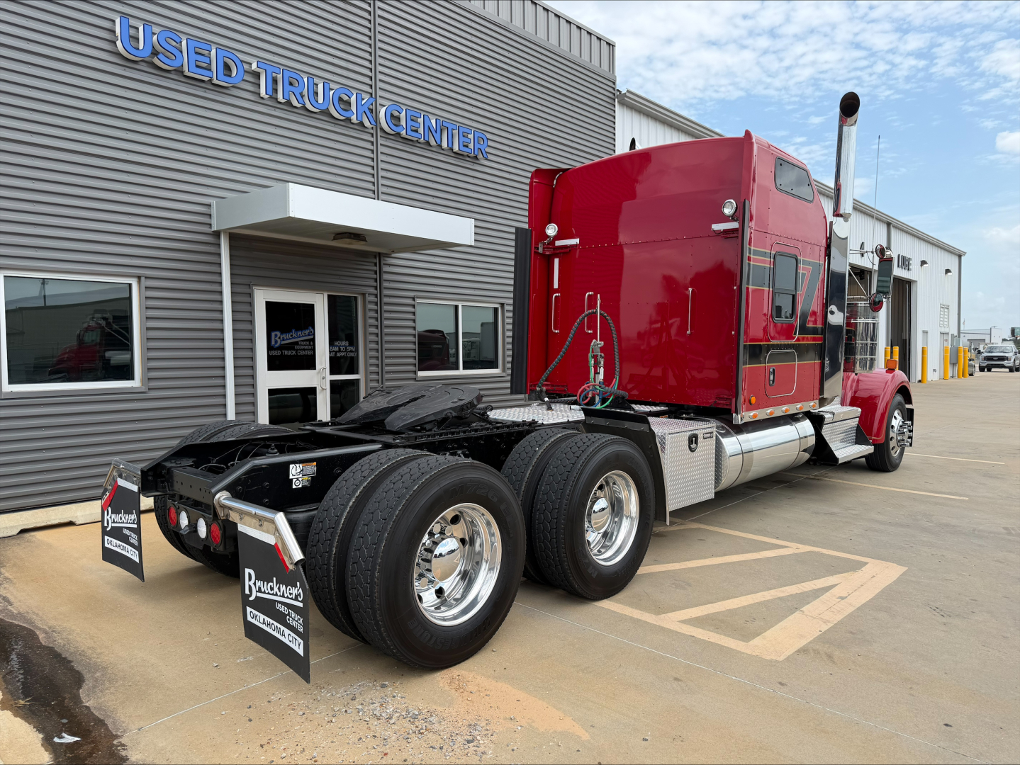 Kenworth W900L truck rear with red sleeper cab and dual rear axles in front of used truck center.