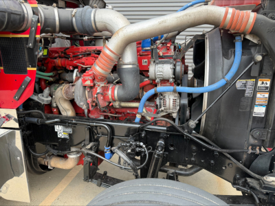 Kenworth W900L engine bay showing red engine block, silver intake pipes, blue hoses, and black chassis with various components.