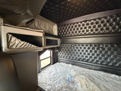 Kenworth W900L sleeper cab interior showing quilted black upholstery, overhead bunk area with storage compartments and window.