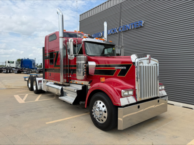 Kenworth W900L sleeper tractor truck in red with chrome grille and exhaust stacks, parked outside a truck center.