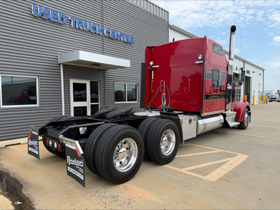 Kenworth W900L truck rear with red sleeper cab and dual rear axles in front of used truck center.