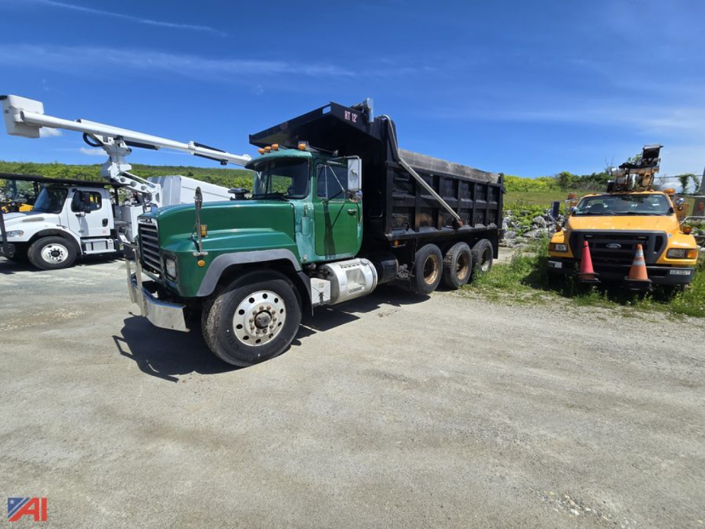 Dump truck with green cab and black dump body, front three-quarter view, on dirt lot.