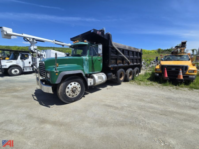 Dump truck with green cab and black dump body, front three-quarter view, on dirt lot.
