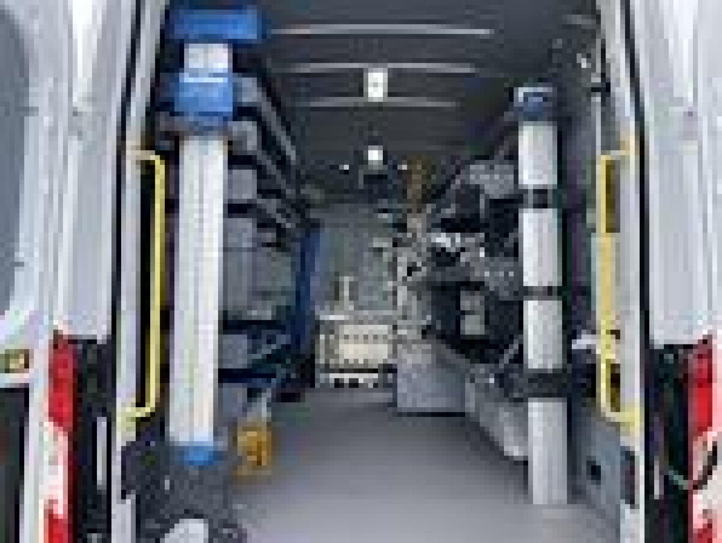 Interior view of a 2024 Ford Transit van cargo area with shelving on both sides, walk-through center aisle, and equipment racks.