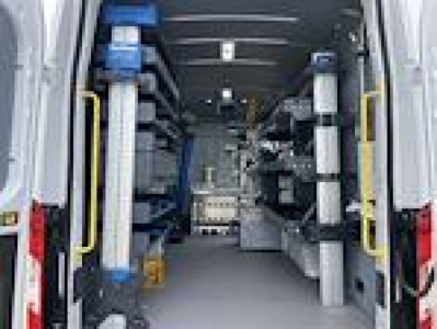 Interior view of a 2024 Ford Transit van cargo area with shelving on both sides, walk-through center aisle, and equipment racks.