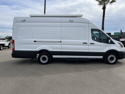 Ford Transit van side view showing cargo area with raised roof and vent on top, white exterior, black bumper and wheels.