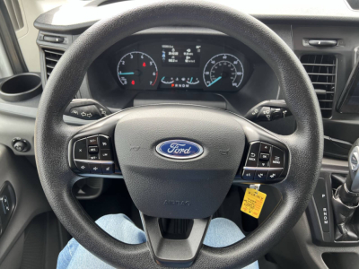 Ford Transit van interior steering wheel and instrument cluster with Ford logo on steering wheel, control stalks visible, yellow key tag hanging.