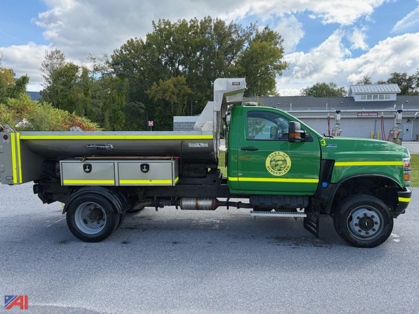 International CV515 dump truck with plow and green cab showing a circular logo on the door and silver/gray dumping bed with compartments